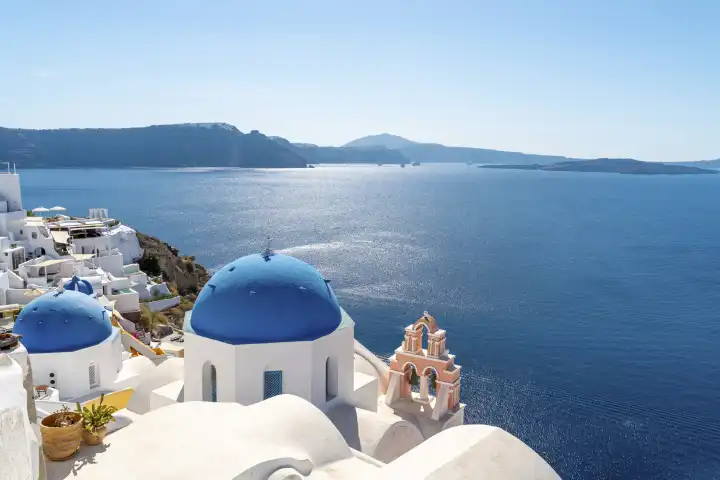 Berühmte Aussicht aus der Stadt Oia auf Santorini in Griechenland. Orthodoxe weiße Kirche mit einer blauen Kuppel als Dach mit einem weißen Kreuz