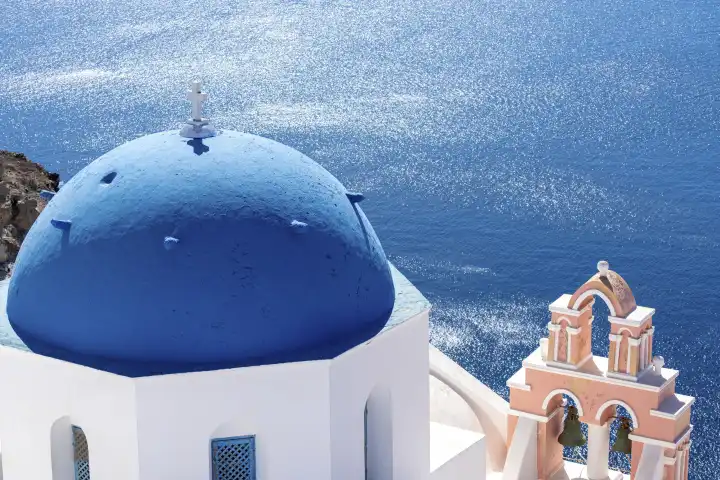 Berühmte Aussicht aus der Stadt Oia auf Santorini in Griechenland. Orthodoxe weiße Kirche mit einer blauen Kuppel als Dach mit einem weißen Kreuz