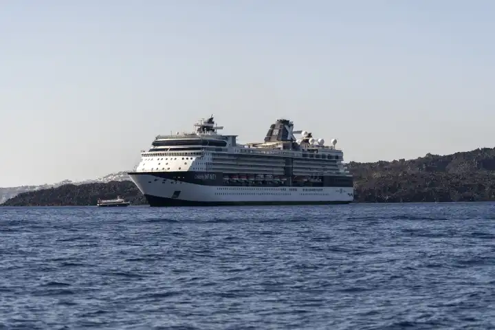 Santorini, Greece - 20 September 2023: The cruise ship of Celebrity Cruises (belongs to Royal Caribbean Cruises) with the ship Celebrity Infinity in the sea in Greece off the island of Santorini