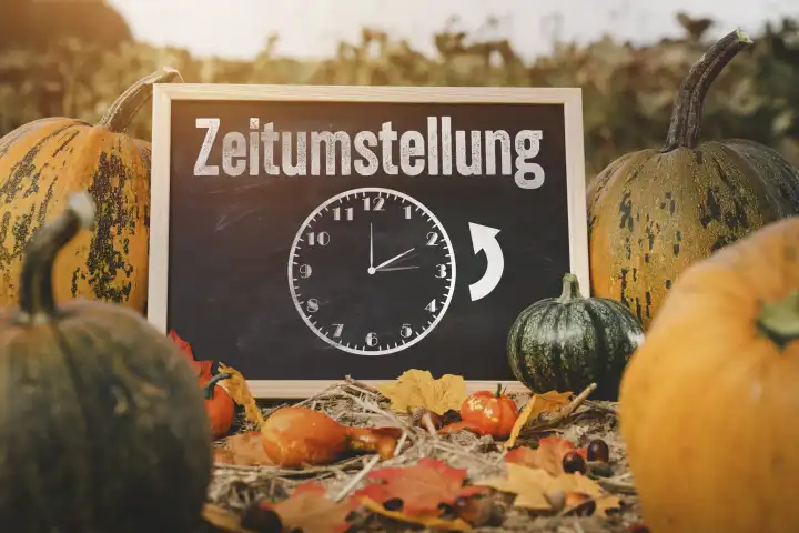 Zeitumstellung von Sommerzeit auf Winterzeit, Tafel auf einem Kürbisfeld bei Sonnenuntergang mit einer Uhr und der Aufschrift: Zeitumstellung FOTOMONTAGE 