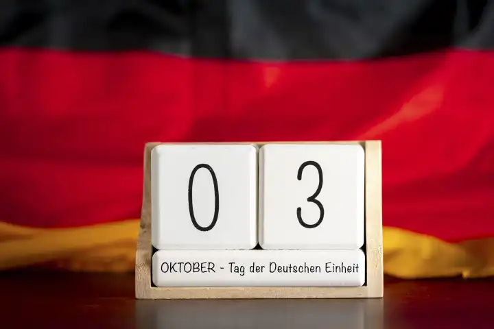 Symbolbild Tag der Deutschen Einheit Feiertag und Brückentag in Deutschland. Würfel Kalender mit 3 Oktober vor Deutschland Landesflagge FOTOMONTAGE