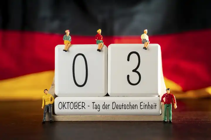 Augsburg, Bavaria, Germany - 30 September 2023: Iconic German Unity Day holiday and bridge day in Germany. Cube calendar with 3 October and figures in front of Germany national flag PHOTOMONTAGE