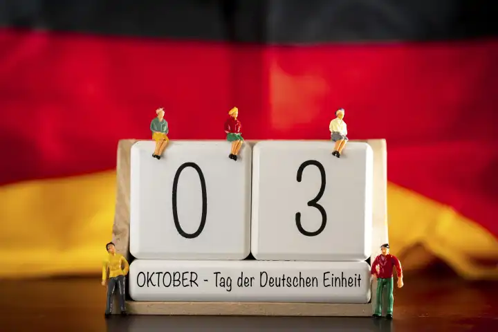 Augsburg, Bavaria, Germany - 30 September 2023: Iconic German Unity Day holiday and bridge day in Germany. Cube calendar with 3 October and figures in front of Germany national flag PHOTOMONTAGE