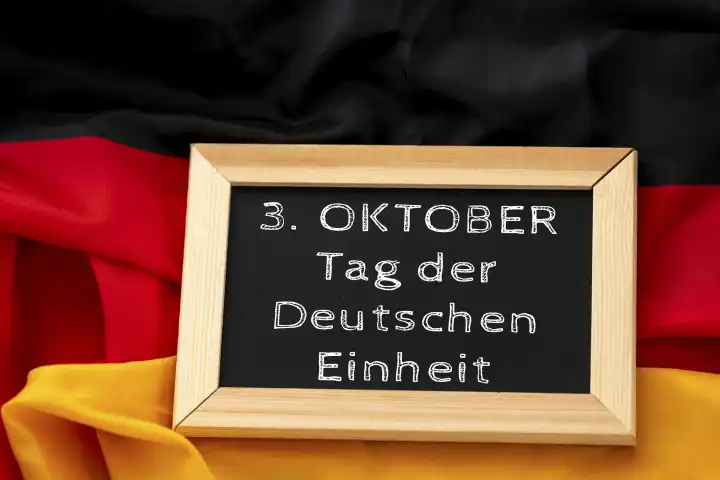 Tafel auf Deutschland Landesflagge in Schwarz Rot Gold mit aufschrift: 3. Oktober Tag der Deutschen Einheit. Feiertag FOTOMONTAGE