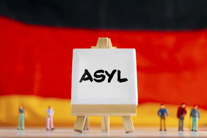 Deutschlandflagge mit Miniatur Menschen und einer Leinwand mit Aufschrift: Asyl FOTOMONTAGE