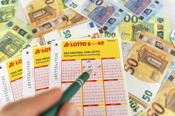 Lotto 6 aus 49 Spielscheine auf Euro Bargeld Scheinen. Glücksspiel Lotterie, Hand füllt Tippfelder aus mit Kugelschreiber
