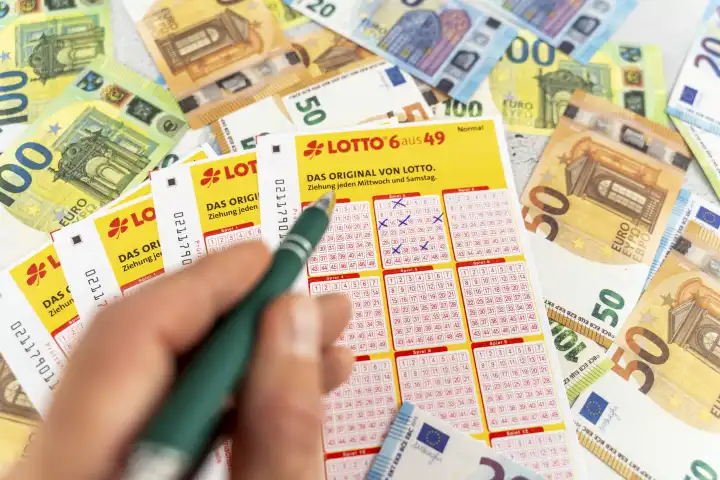 Lotto 6 aus 49 Spielscheine auf Euro Bargeld Scheinen. Glücksspiel Lotterie, Hand füllt Tippfelder aus mit Kugelschreiber