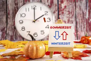 Zeitumstellung, Uhr mit Herbstblättern und einer Tafel mit Aufschrift: Sommerzeit und Winterzeit FOTOMONTAGE