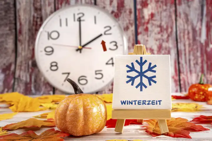 14 October 2023: Time change from summer time to winter time, clock with autumn leaves and a board with inscription: Winter time with snow symbol PHOTOMONTAGE