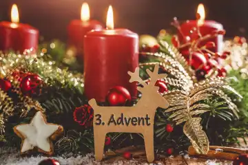 Adventskranz mit brennenden Kerzen zu Weihnachten mit einem Schild in Rentier Form mit Text: 3. Advent (Dritter Advent). Adventszeit Konzept FOTOMONTAGE