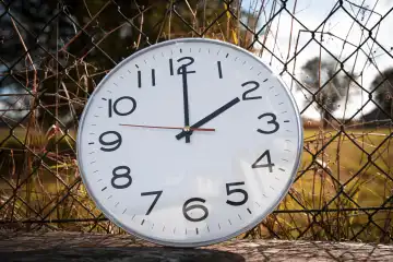Symbolbild Zeitumstellung von Sommerzeit auf Winterzeit. Uhr zwischen Laub im Herbst mit dem Zeiger auf Uhrzeit 2 Uhr