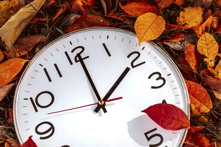Augsburg, Bavaria, Germany - 16 October 2023: Symbolic image time change from summer time to winter time. Clock between foliage in autumn with the hand on time 2 o'clock