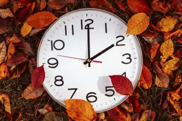 Symbolbild Zeitumstellung von Sommerzeit auf Winterzeit. Uhr zwischen Laub im Herbst mit dem Zeiger auf Uhrzeit 2 Uhr
