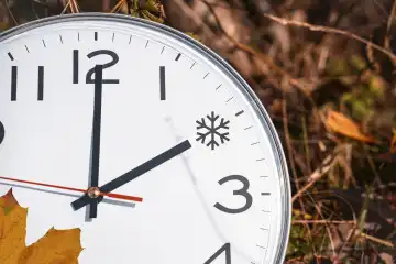 Symbolbild Zeitumstellung von Sommerzeit auf Winterzeit. Uhr liegt zwischen Laub im Herbst mit dem Zeiger auf Uhrzeit 2 Uhr. Eis Symbol als Zeit FOTOMONTAGE