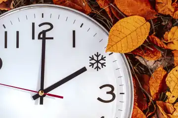 Augsburg, Bavaria, Germany - 16 October 2023: Symbolic image time change from summer time to winter time. Clock lies between foliage in autumn with the hand on time 2 o'clock. Ice symbol as time PHOTOMONTAGE