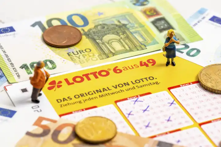 Miniaturfiguren stehen auf einem Lotto 6 aus 49 Spielschein mit Euro Bargeld Scheinen und Münzen. Glücksspiel Lotterie 