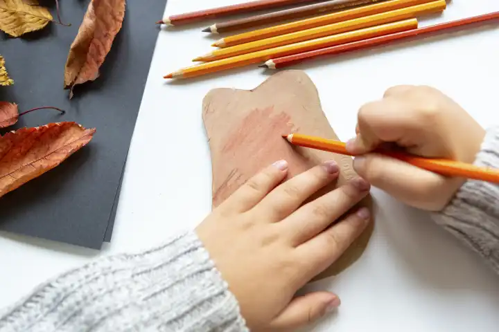 Kinderspaß mit Herbstlaub: Kreatives Basteln zu Hause. Ein Kind bastelt einen Igel aus Pappe. Hände malen mit Farbe, Pinsel und Stiften das Bild aus