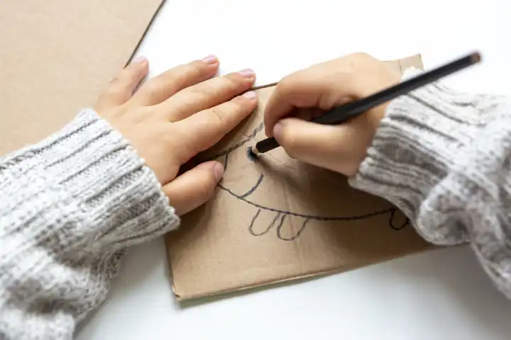 Kinderspaß mit Herbstlaub: Kreatives Basteln zu Hause. Ein Kind bastelt eine Kollage von einem Igel aus Pappkarton, Zeichnet diesen auf und Malt ihn mit bunten Stiften und Farbe aus 