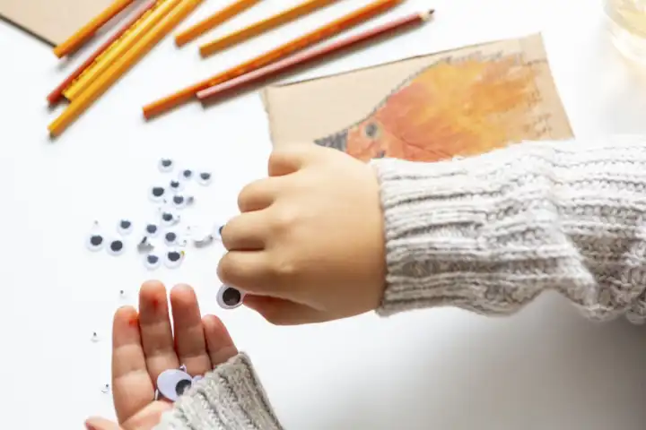 Kinderspaß mit Herbstlaub: Kreatives Basteln zu Hause. Ein Kind bastelt eine Kollage von einem Igel aus Pappkarton, Zeichnet diesen auf und Malt ihn mit bunten Stiften und Farbe aus 