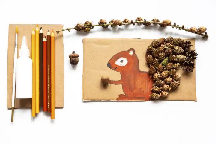 Kinderspaß mit Herbstlaub: Kreatives Basteln zu Hause. Eine Kollage von einem Eichhörnchen mit Tannenzapfen verziert. Bunte Stifte und Kleber