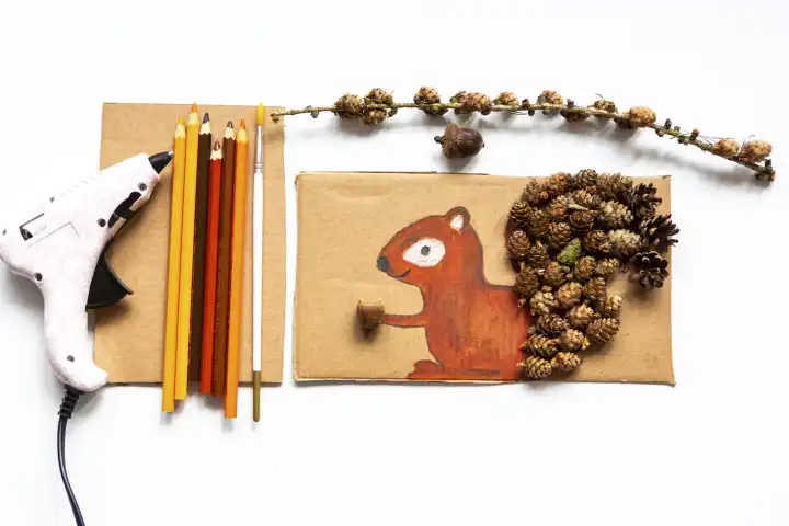 Kinderspaß mit Herbstlaub: Kreatives Basteln zu Hause. Eine Kollage von einem Eichhörnchen mit Tannenzapfen verziert. Bunte Stifte und eine Heißklebepistole 
