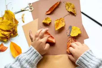 6 October 2023: Children's fun with autumn leaves: creative crafts at home. A child crafts with blank paper and cardboard and colorful leaves in autumn