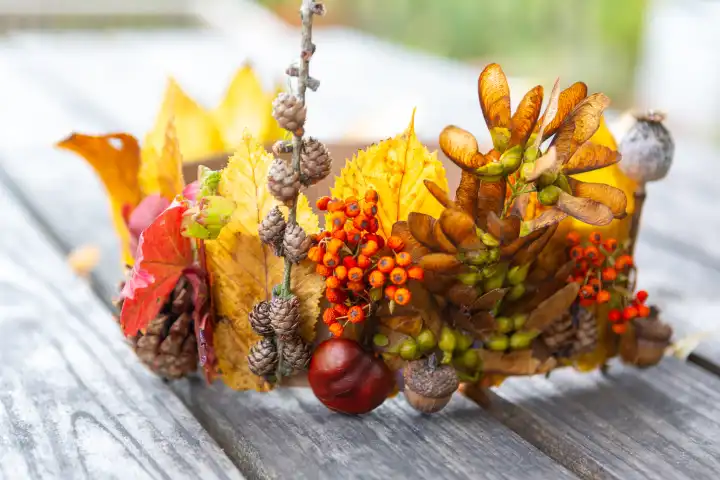 Kinderspaß mit Herbstlaub: Kreatives Basteln im Herbst. Selbstgemachte Krone aus bunten Blättern, Eicheln und Beeren