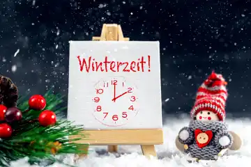 Winterzeit ! Leinwand mit Uhr und einen kleinen Schneemann mit Herz in Schnee. Symbolbild Zeitumstellung FOTOMONTAGE