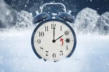 Zeitumstellung von Sommerzeit auf Winterzeit. Ein mit Schnee bedeckter Wecker in einer Winterlandschaft und einer Sonne und einem Eis Symbol für 2 und 3 Uhr. Uhr zurückstellen Konzept FOTOMONTAGE