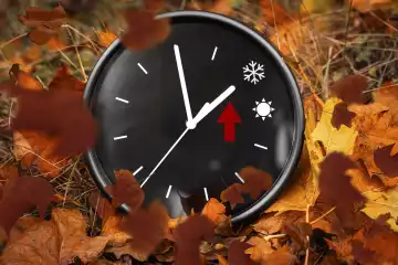 Uhr liegt im Herbst im Laub mit einer Sonne und einem Schnee Symbol, Zeitumstellung von Sommerzeit auf Winterzeit Konzept FOTOMONTAGE