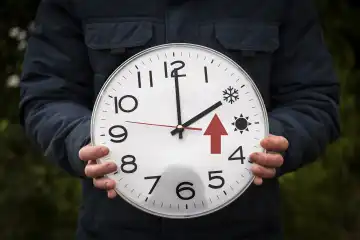 Mann hält große runde Uhr mit Sommer und Winterzeit in der Hand. Ein großer roter Pfeil steht für die Uhr zurückstellen FOTOMONTAGE