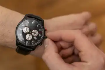 Ein Mann stellt die Uhrzeit an seiner Armbanduhr ein. Zeitumstellung Konzept