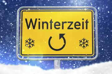 Ein gelbes Schild mit der Aufschrift Winterzeit und zwei Schneeflocken darauf, vor einem Hintergrund aus fallendem Schnee und blauem Himmel. Zeitumstellung im Oktober FOTOMONTAGE