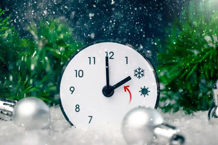27 October 2023: Symbolic image time change clock with an arrow from daylight saving time to winter time in snowy landscape during snowfall PHOTOMONTAGE