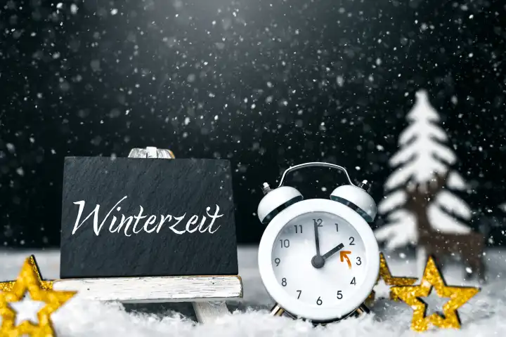 27 October 2023: Alarm clock in winter landscape next to sign with text winter time. Symbol image time change in autumn PHOTOMONTAGE
