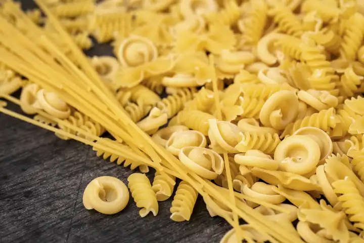 Various types of pasta noodles on a black wooden background. Farfalle, spaghetti, fusilli