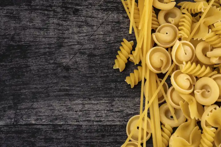Various types of pasta noodles on a black wooden background. Farfalle, spaghetti, fusilli