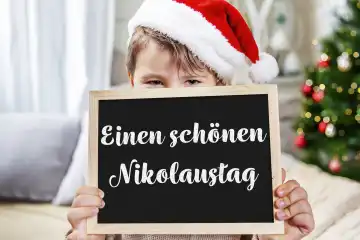 November 22, 2023: A happy St. Nicholas Day greeting on a sign is held by a child with a Christmas hat in a living room decorated for Christmas PHOTOMONTAGE