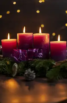 November 24, 2023: Advent season themed picture, four purple candles burning in the dark on an Advent wreath with colorful lights in the background