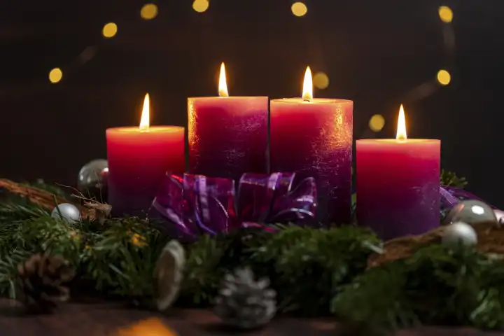 Adventszeit Themenbild, vier lila Kerzen brennen bei dunkelheit auf einem Adventskranz mit bunten Lichtern im Hintergrund