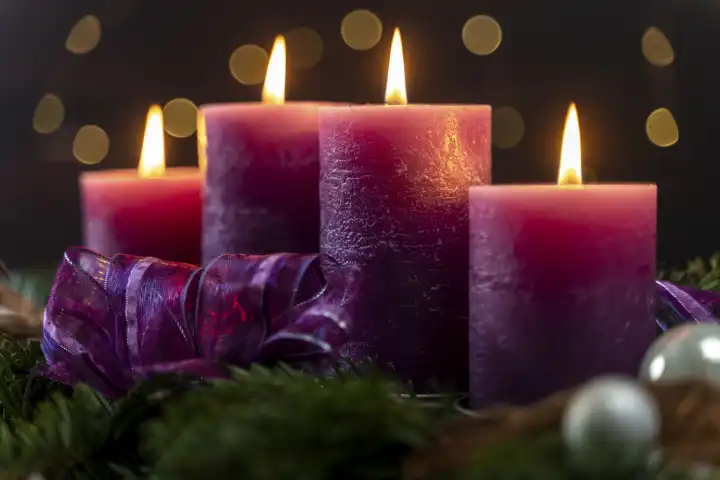 Adventszeit Themenbild, vier lila Kerzen brennen bei dunkelheit auf einem Adventskranz mit bunten Lichtern im Hintergrund
