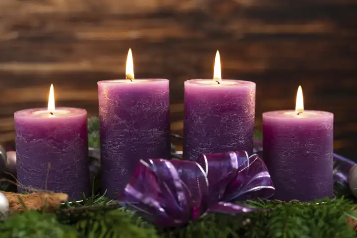 November 24, 2023: Advent wreath with four burning purple candles for the fourth Sunday of Advent in front of a rustic wooden background