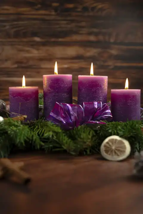 Adventskranz mit vier brennenden Lila Kerzen zum vierten Adventssonntag vor rustikalem Holz Hintergrund