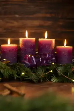 Adventskranz mit vier brennenden Lila Kerzen zum vierten Adventssonntag vor rustikalem Holz Hintergrund