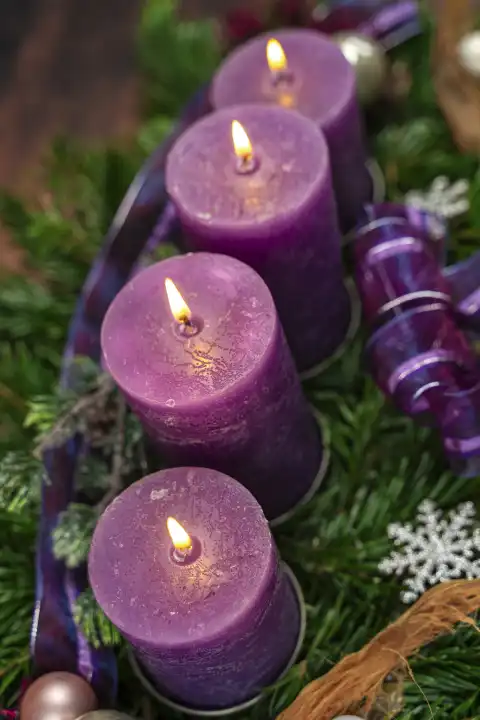November 24, 2023: Advent wreath with four burning purple candles for the fourth Sunday of Advent in front of a rustic wooden background