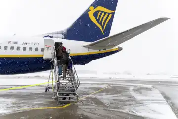 Wintereinbruch und Schneechaos auf dem Flughafen in Bayern, Passagiere steigen in ein Flugzeug der Airline Ryanair bei Schneefall