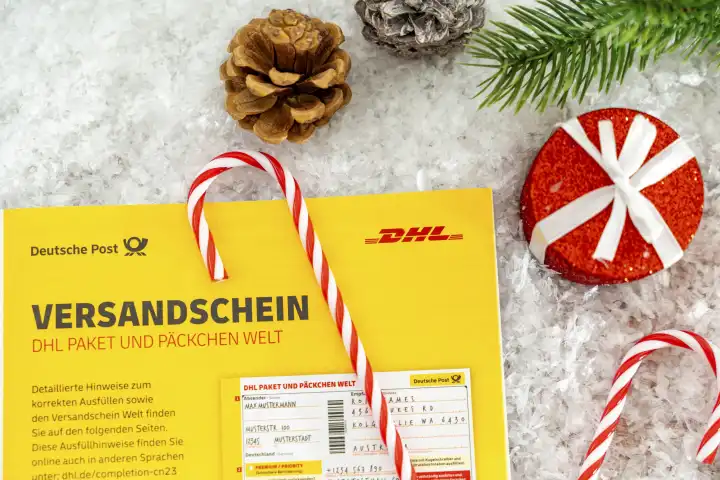 DHL Paket und Päckchen Versandschein neben Dekoration zu Weihnachten, einem roten verpackten Geschenk