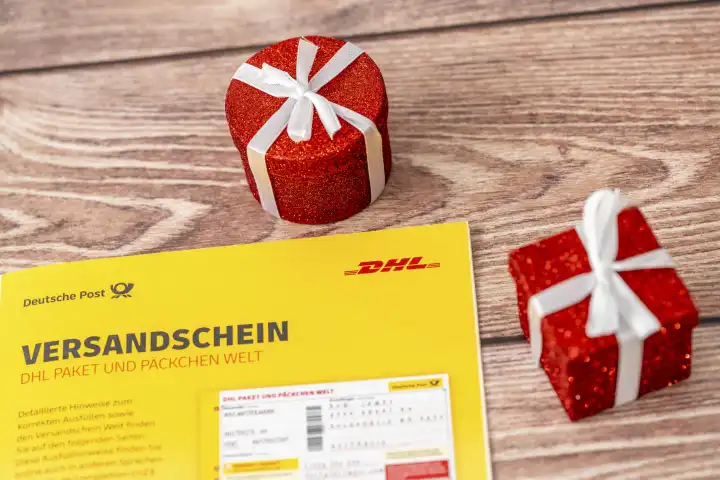 DHL Paket und Päckchen Versandschein neben Dekoration zu Weihnachten, einem roten verpackten Geschenk