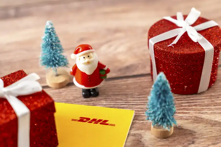 Augsburg, Bavaria, Germany - December 15, 2023: DHL parcel and parcel shipping label next to decoration for Christmas, a red wrapped gift