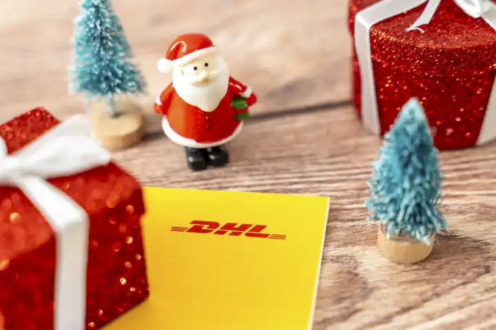 Augsburg, Bavaria, Germany - December 15, 2023: DHL parcel and parcel shipping label next to decoration for Christmas, a red wrapped gift